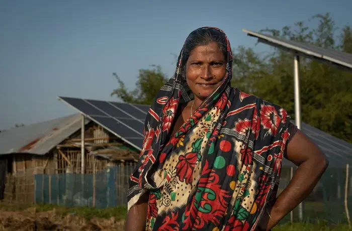 A woman poses in front of the solar panels helping to power her farm